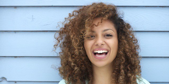 woman laughing blue background after having cosmetic dentistry treatment